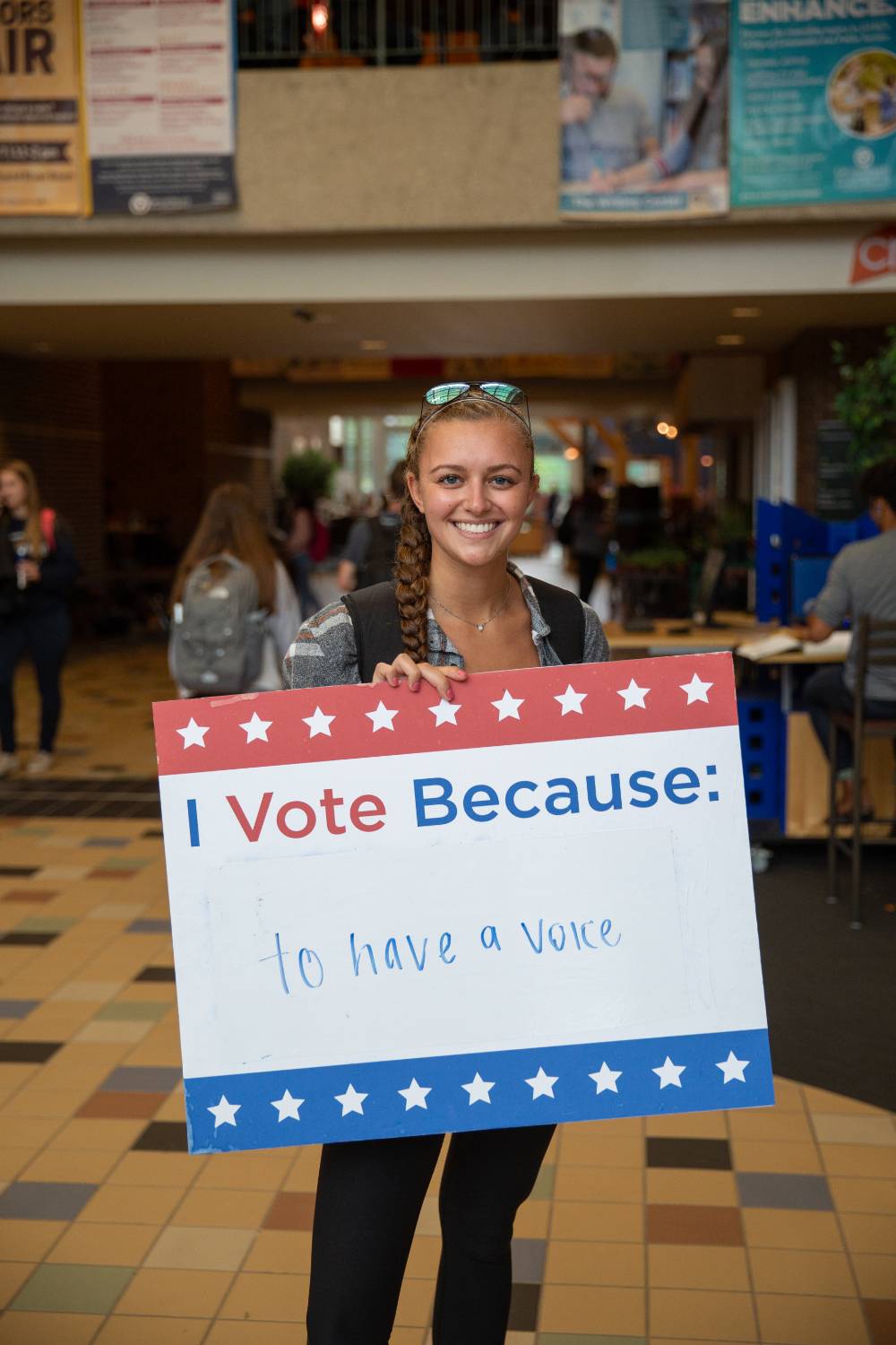 Student holding sign titled "I vote because: to have a voice"